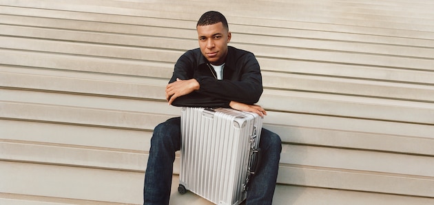 Kylian Mbappé sitting with a Classic Cabin suitcase in silver