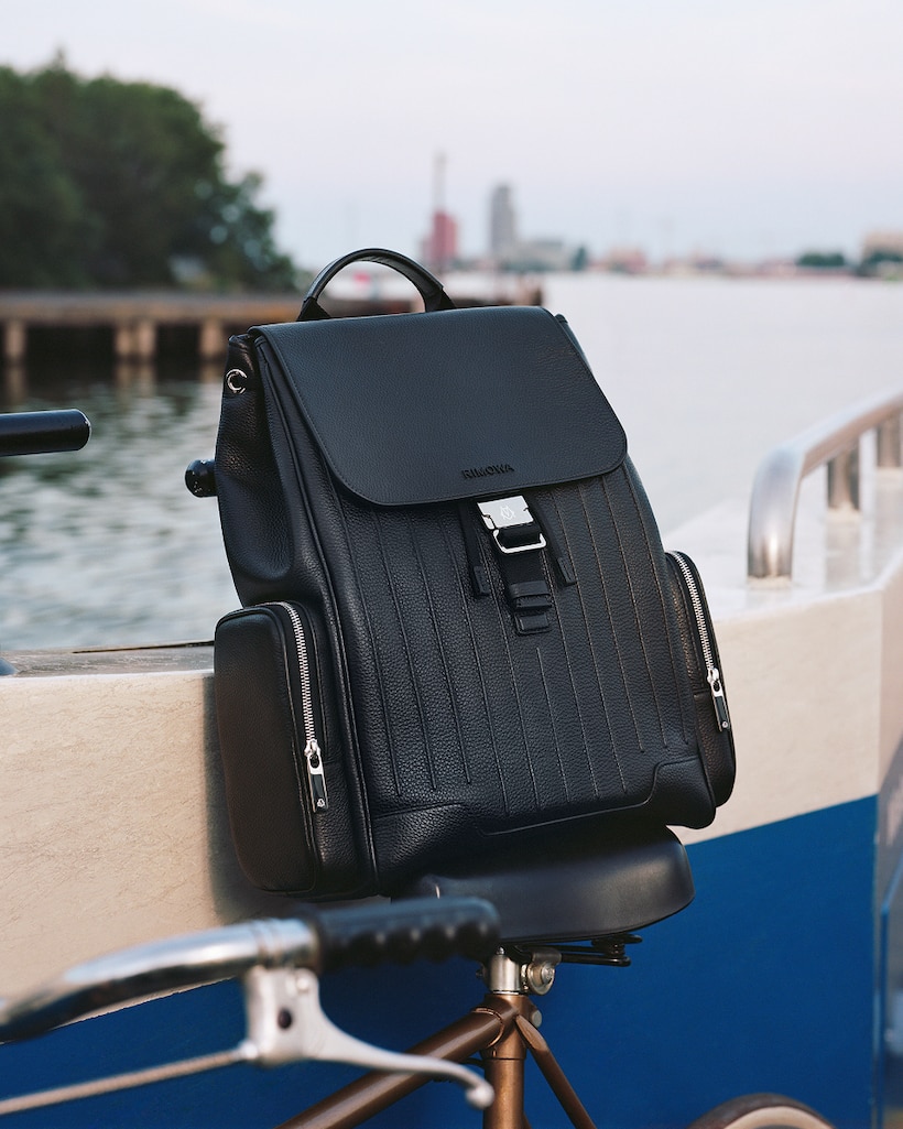Black RIMOWA backpack placed on a blue surface outdoors.